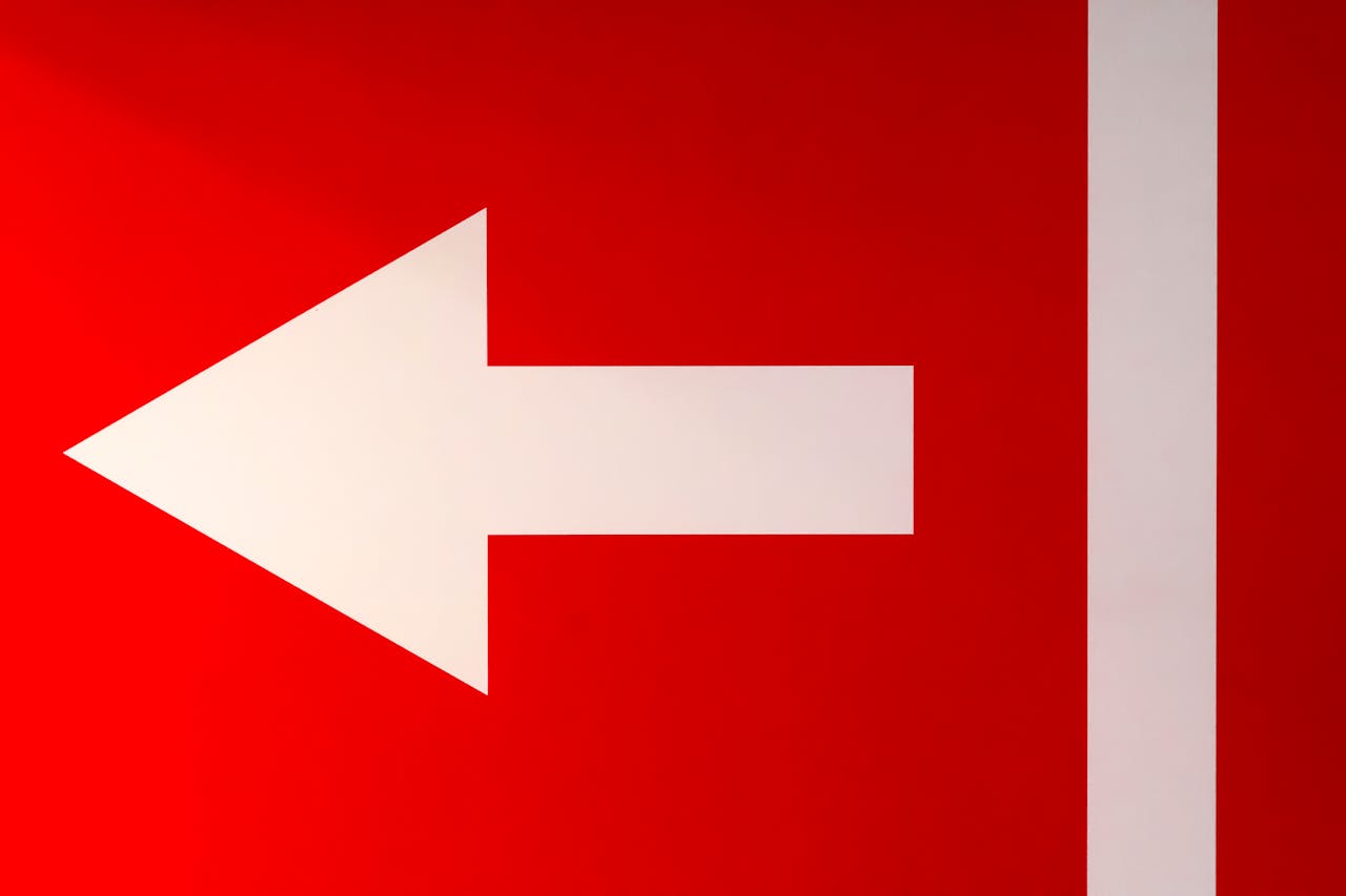White arrow pointing left on a bold red background, symbolizing direction.